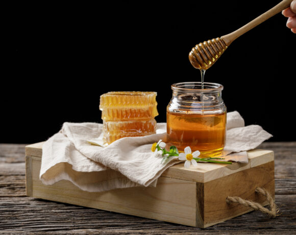 Pszczoła miodna w słoiku i plastrze miodu z czerpakiem miodu i kwiatem na drewnianym stole, produkty pszczele według koncepcji organicznych składników naturalnych, miejsce na tekst